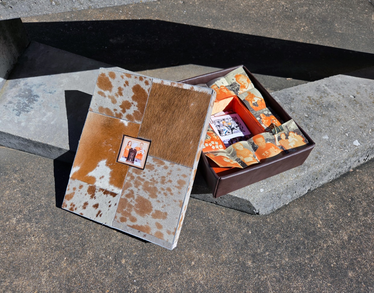 The cowhide lid lifted off the Burnt Orange Saturdays box, collaged photographs inside