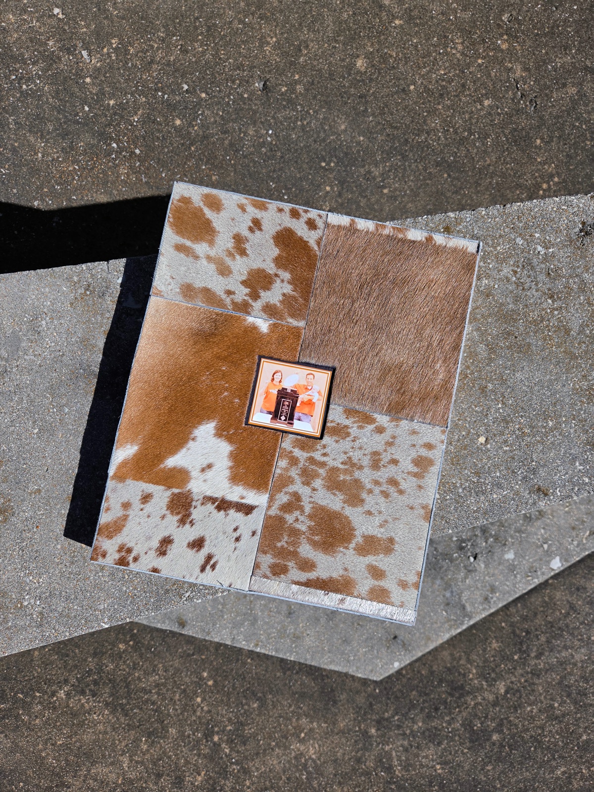 The lid seen from above: four panels of cowhide around a small framed photograph of the family in burnt orange